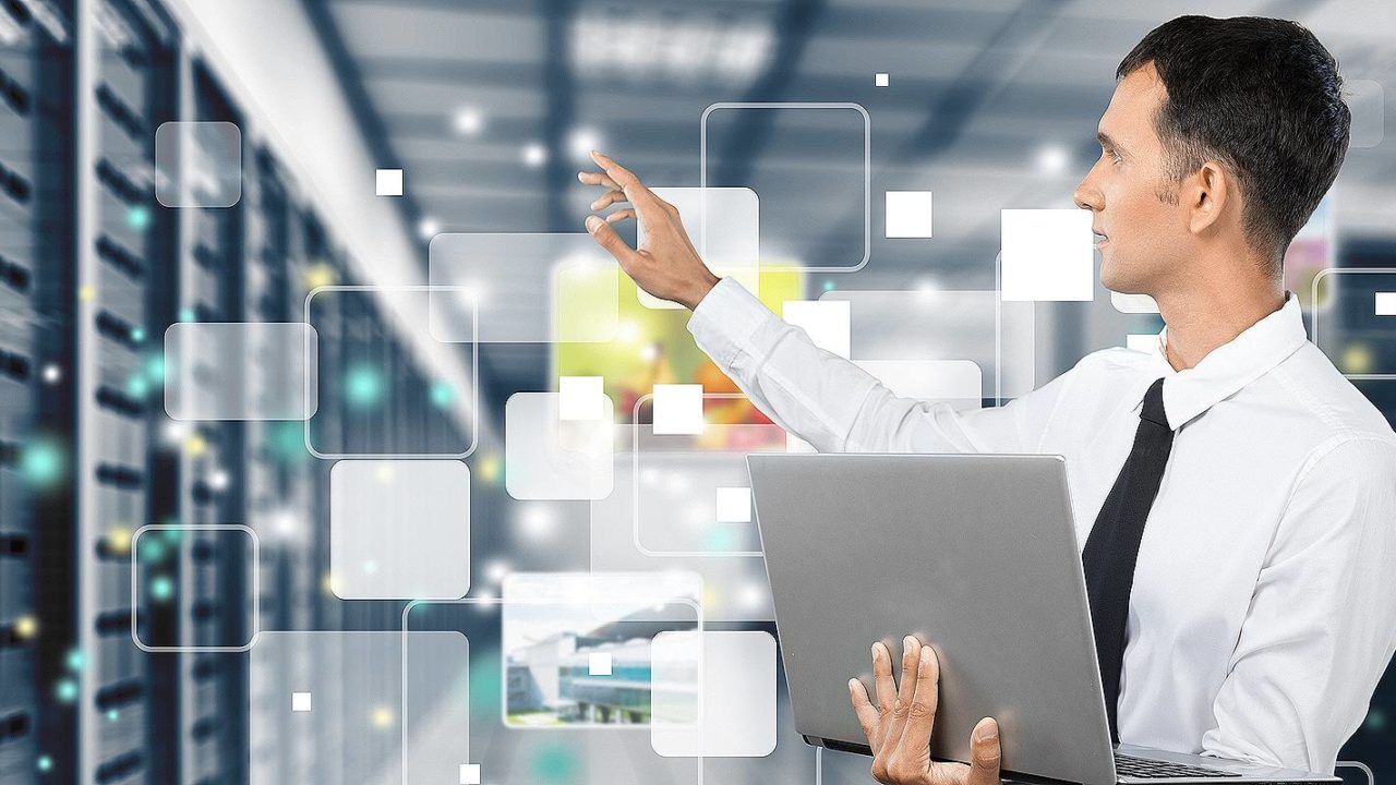 A representational image of Managed IT services. A person holding a laptop is standing on the backdrop of a data center