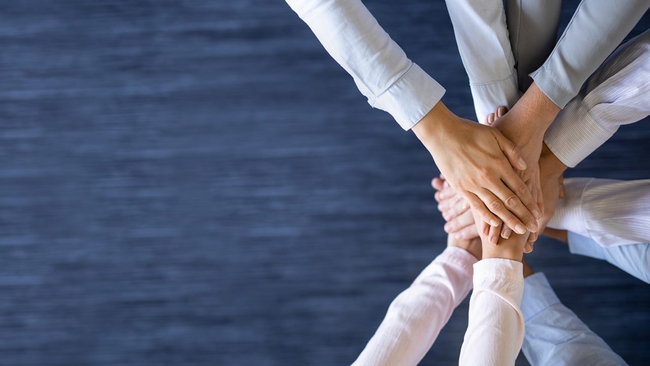 Stack of hands signifying unity and teamwork. MSPs can support in-house IT teams