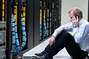 man calling on a smartphone and looking at a laptop computer in a network data center